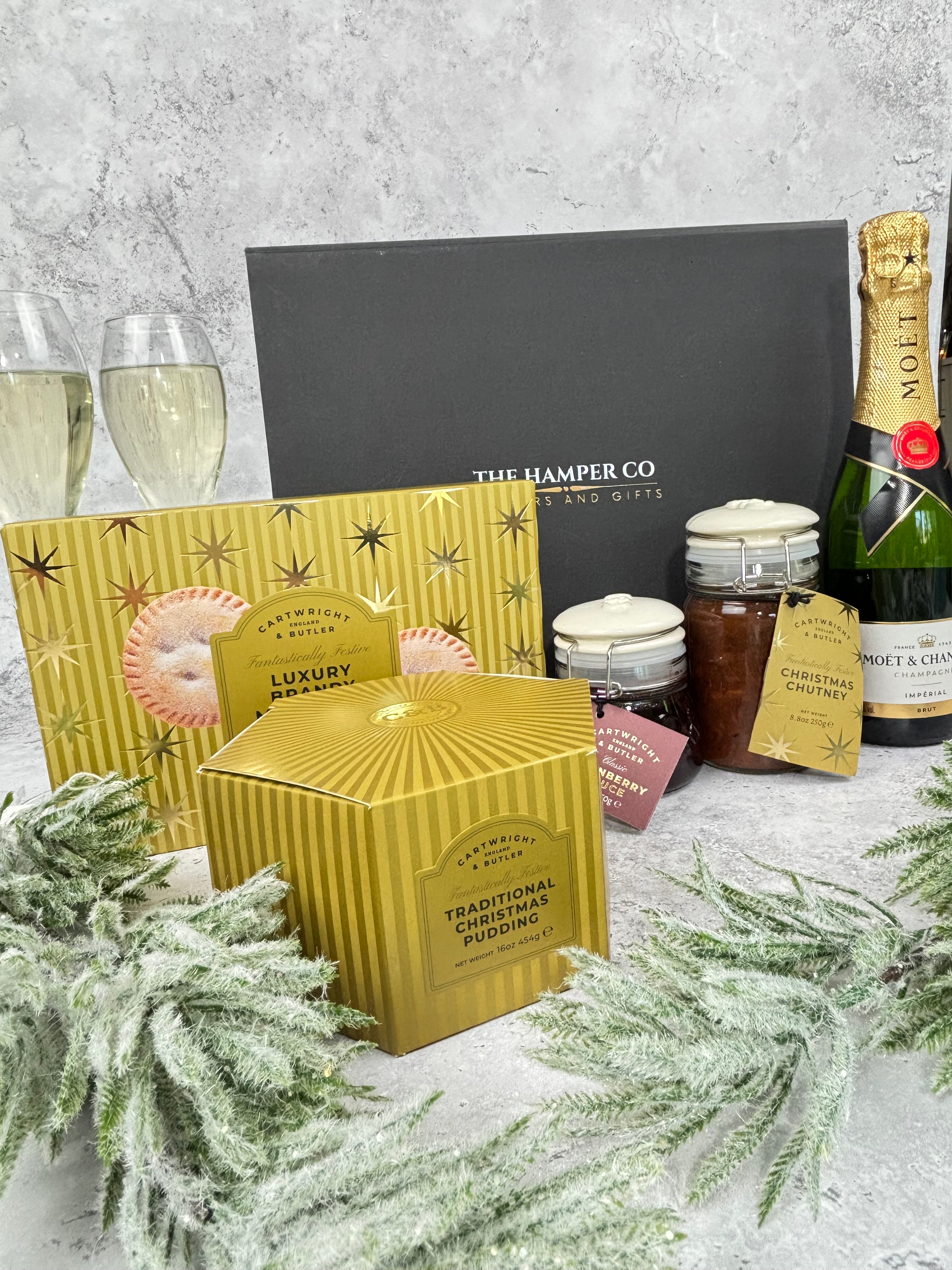 A Christmas Hamper gift box, showing moet & chardon Champagne, Cartwright & butler Christmas range including, brandy mince pies, cranberry sauce, Christmas chutney & traditional Christmas pudding.