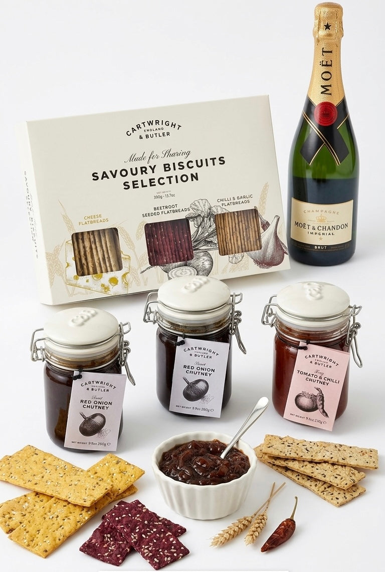 Bottle of Moet champagne with a box of savoury biscuits, jars of preserves, and crackers on a white background.