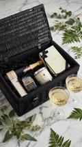 luxury hamper basket with jo malone candle and reed difuser, hotel chocolat salted puddles and macarons. moet chardon champagne with champagne fluts filled on a marble background