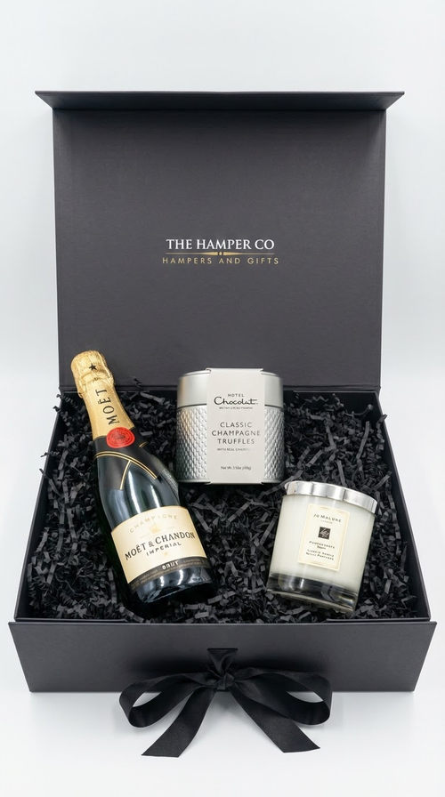 luxury champagne gift bx with jo malone andle and champagne truffles from hotel chocolat, black shredded paper on a white professional background.