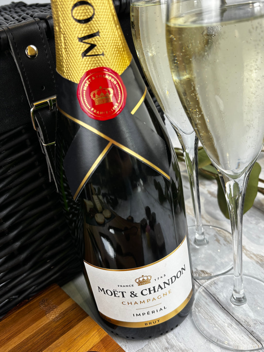 A bottle of Moët & Chandon Impérial Brut champagne next to a filled champagne flute, with a black woven bag in the background.